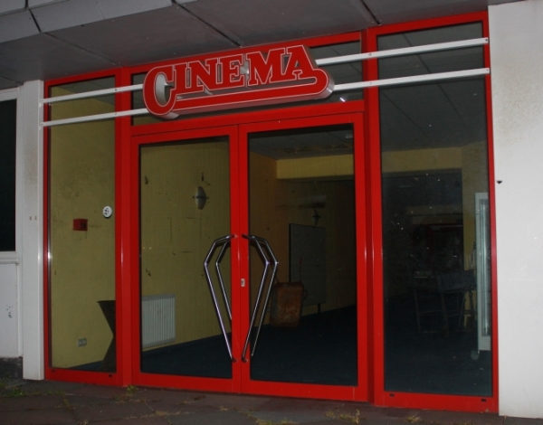 Foto mit einer Aufnahme von der ehemaligen Eingangstür; über der Tür ist die alte Leuchtreklame mit dem Logo des CINEMA zu sehen.