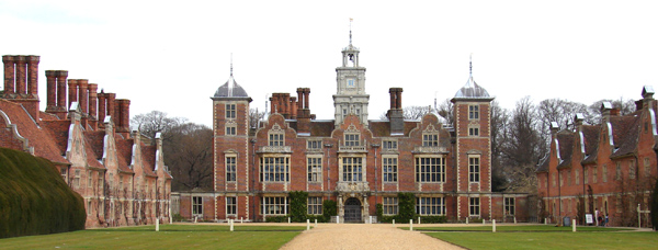 Picture of Blickling Hall, a red-bricked Jacobean mansion with a seven bay front and corner turrets; a painted, timber-clad clock tower; gravel and lawn forecourt flanked by service wings and ancient yew hedges.