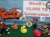 “Celebrating MaxB’s 10,000 TB” Tour Group Geopigs presented MaxB with the Big Orange Helicopter in recognition of their having taken 10,000 TBs on tour.  The BOH is shown hovering over each tour group after departing MaxB&#8217;s latest transport.  Shown are TB&#8217;s:  Monkey Squadron-Red Leader, Nemo the Racing Fish, Dewey Duck, Entosco Bug, LZ33&#8217;s Alabama Coin, Little Net River (AK) Red jeep, Someone You Know, Troy OH Diabetes TB, T-Bonz&#8217;s Racer, and Big Dora.