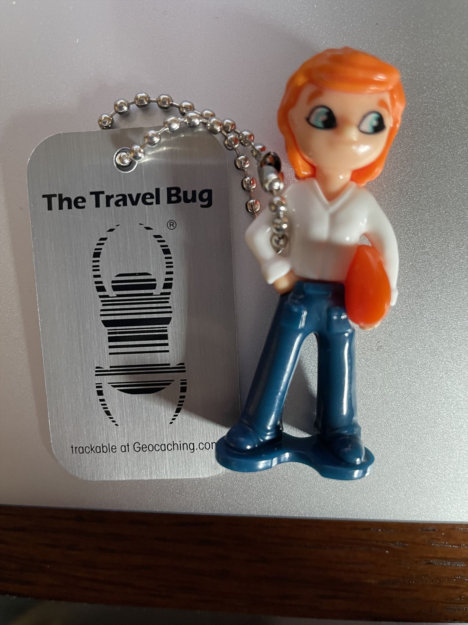 Carina the Explorer is a rectangular metal travel tag with attached small plastic female figure with red hair and blue jeans