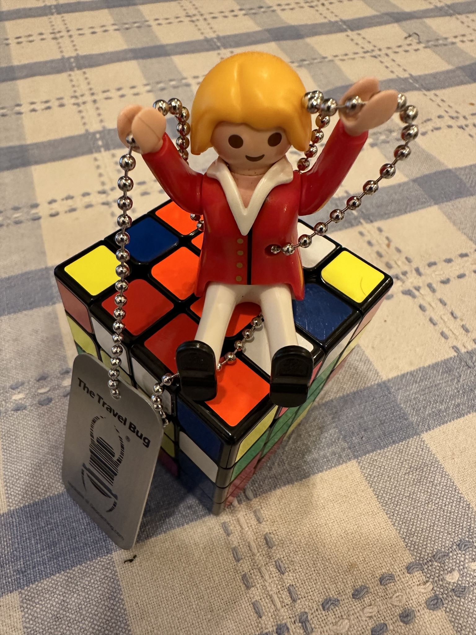 Female playmobil with blonde hair wearing a red jacket sittiing on a 4 by 4 rubiks cube